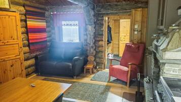 Interior acogedor de una cabaña de troncos con una mesa de comedor de madera, un sofá de cuero, un sillón rojo y una chimenea de piedra.
