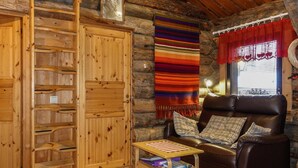 Interior acogedor de una cabaña de madera con una escalera de madera, un sillón de cuero, una mesita con libros y una manta tejida de colores.