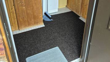 A room with wooden walls, a white door, a black carpet, and a metal doormat.