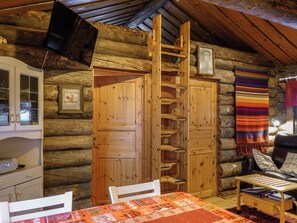 A log cabin interior with a wooden table, chairs, a bookshelf, and a television mounted on the wall. - Hopukka a2 by Interhome (Sodankylä)