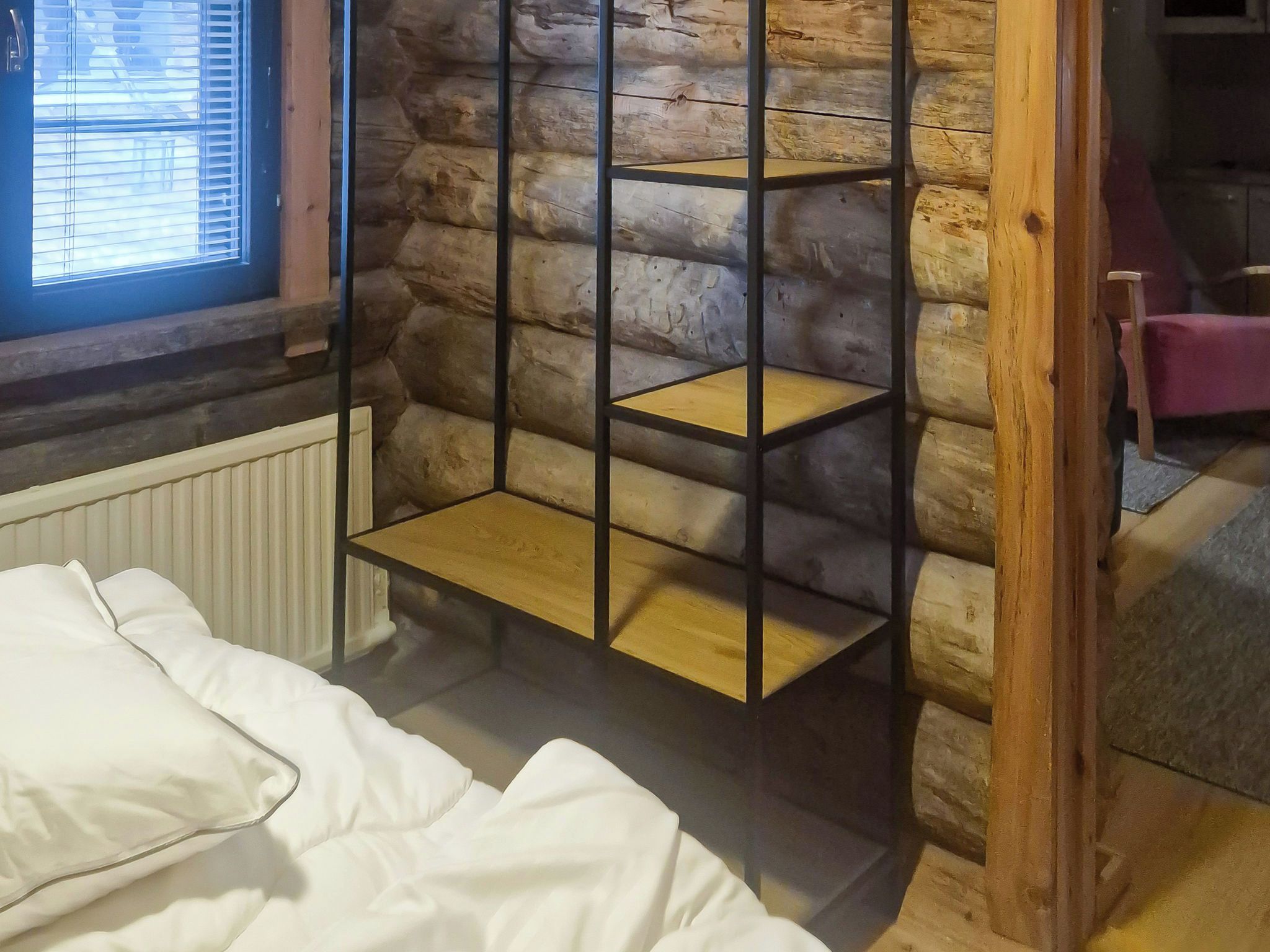 Una habitació amb un llit, una estantària de fusta i una finestra amb persianes.