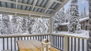A wooden deck with a bench and a lantern, overlooking a snowy landscape with trees and a cabin. - Kaukonraitti 4 c 2 by Interhome (Kuusamo)