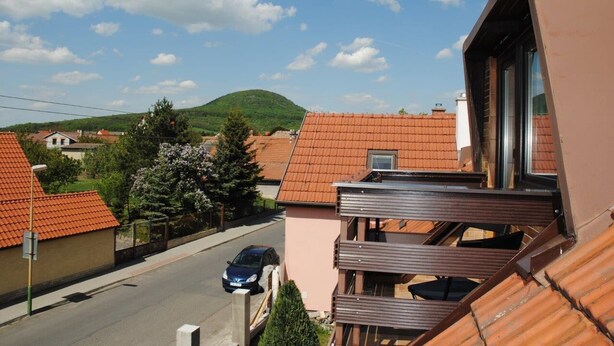Zona residencial com casas de telhado em terracota, céu claro e paisagem montanhosa ao fundo.