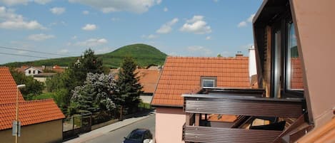 A residential area with terracotta-roofed houses, a clear sky, and a hilly landscape in the background.