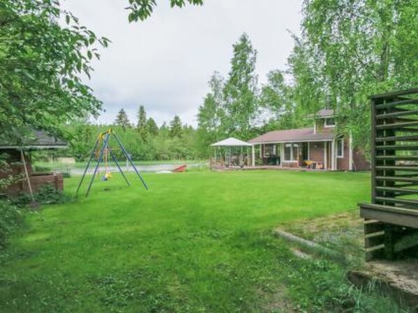 A backyard with a swing set, a covered patio, and a wooden deck.