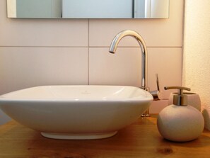 Un lavabo blanc, de style moderne, avec un robinet contemporain, un distributeur de savon et un miroir au-dessus.