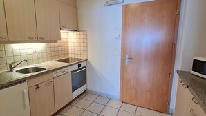Eine kleine Küche mit Spüle, Herd und Geschirrspüler, Holzschränken und einer gefliesten Spritzschutzwand.