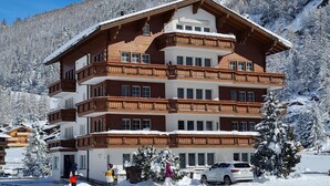 Ein mehrstöckiges Hotel mit Holzbalkonen, ein Ski-Hang im Hintergrund und verschneite Umgebung.