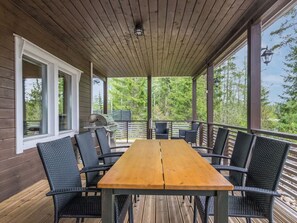 A covered outdoor dining area with a wooden table and chairs, a grill, and a view of trees. - Lammassaari by Interhome (Ikaalinen)