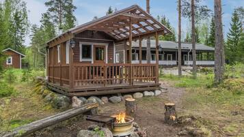 A cabin with a wooden deck, a fire pit, and a covered porch.