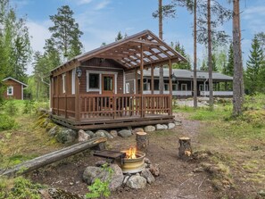 Mökki, jossa on puinen terassi, nuotiopaikka ja katettu kuisti.