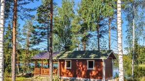Een houten hut met een terras en een klein veranda, omringd door hoge bomen en een meer.