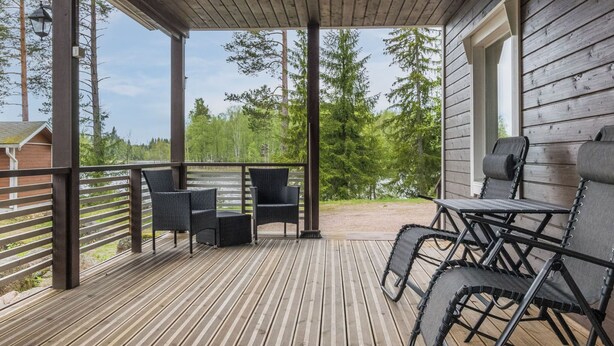 Een overdekt terras buiten, met houten vloer, metalen hekwerk en tuinmeubilair.
