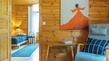 A wooden interior with a bed, a chair, a table, and a painting on the wall.