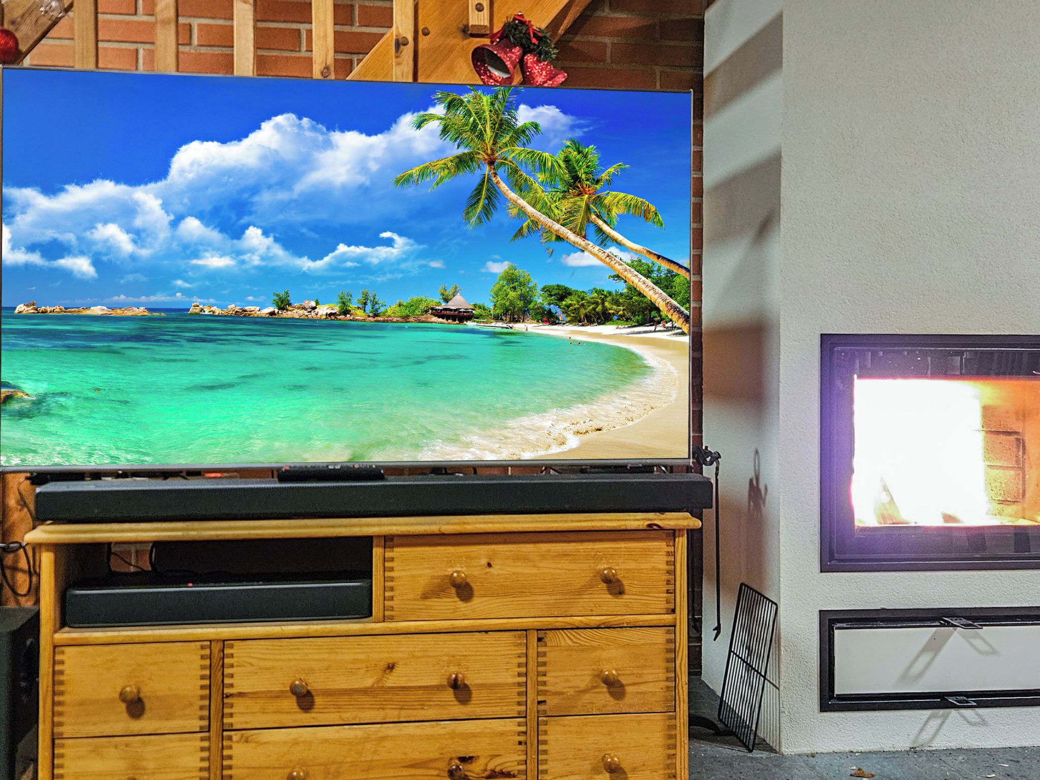 A television displaying a beach scene with clear turquoise water, a palm tree, and a wooden structure.