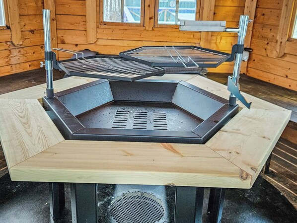 Ein sechseckiger Grill für den Außenbereich mit einem Metallrost, der von Metallständern auf einer Holzplattform gehalten wird.
