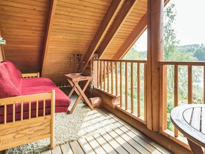 A wooden deck with a red sofa and a small table, overlooking a natural landscape.