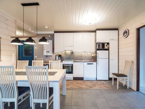 Moderni keittiö, jossa on valkoiset kaapit, ruokailutila puupöydällä ja -tuoleilla sekä pieni jääkaappi.