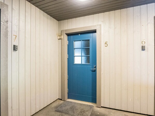 Uma porta azul com uma janela, numerada 5, em um quarto com paredes brancas e piso de concreto.