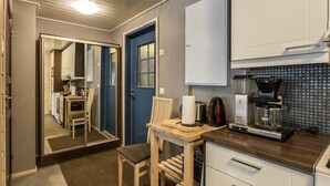 Eine kompakte Küche mit Kaffeemaschine, Toaster und Mikrowelle. Es gibt einen Holztisch mit Stuhl, einen weißen Schrank und einen Spiegel an der Wand.