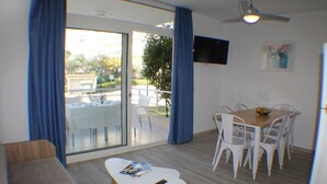 A room with a dining table, chairs, a sofa, a TV mounted on the wall, and a sliding glass door leading to an outdoor area. - Rescator Resort 202 - Two Bedroom Apartment, Sleeps 6 (Roses)
