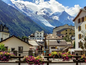 A mountain village with traditional buildings, a bridge with flower boxes, and a backdrop of snow-capped mountains.