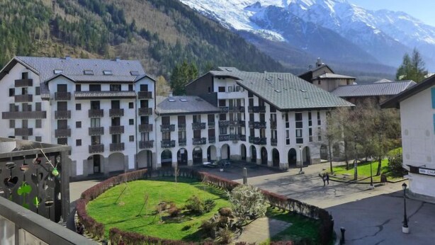 Un cortile con edifici, un prato verde e montagne innevate sullo sfondo.