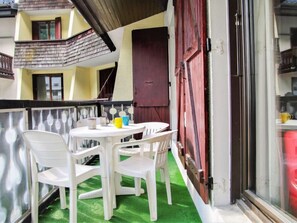 A balcony with a table and chairs, a red door, and a window with a curtain.