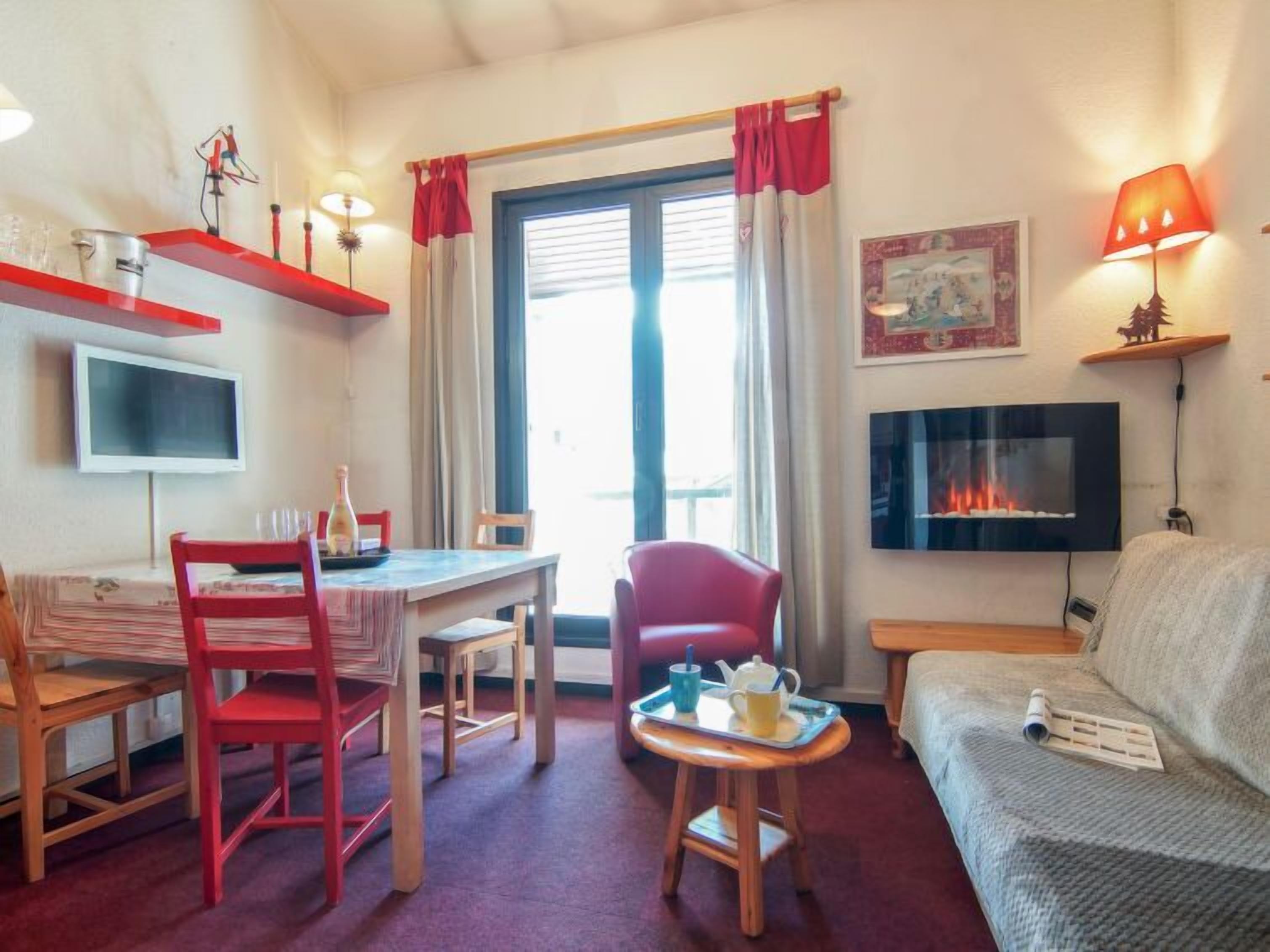 A cozy room with a dining table, chairs, a sofa, a TV, a fireplace, and a window with curtains.