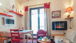 Una stanza accogliente con un tavolo da pranzo, sedie, un divano, una televisione, un caminetto e una finestra con tende.