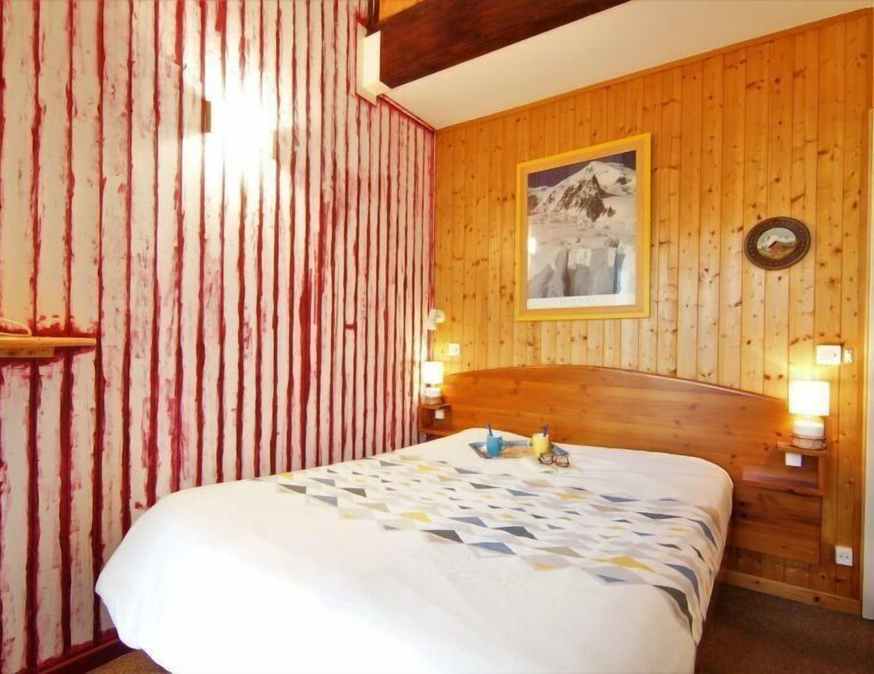 Een hotelkamer met een houten hoofdeinde, een bed met een beddegoed met een patroon, een lijst met een afbeelding aan de muur, en twee nachtlampjes.
