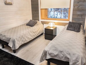 A bedroom with two beds, a nightstand, a lamp, and a window with a view of snow-covered trees.