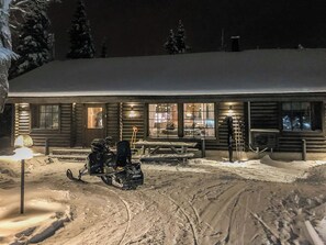 Una cabaña de troncos con techo nevado, un trineo y un perro de trineo.