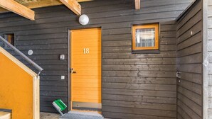 Una cabaña de madera con puerta número 18, un ventanal pequeño y un escalón metálico que lleva a la entrada.