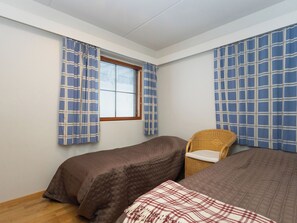 Une chambre avec deux lits, une chaise en osier et une fenêtre avec des stores.