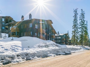 Un edificio de varios pisos con una chimenea destacada, una entrada cubierta de nieve y un cielo despejado.