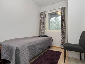 Habitació petita amb un llit individual, una finestra, una cadira i una catifa morada.