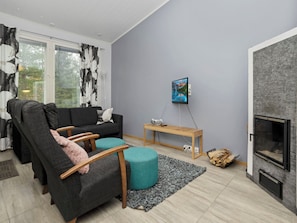 Un salon moderne avec un canapé, un pouf et une petite table sur laquelle se trouve une radio. On y trouve également une cheminée et un tableau accroché au mur.