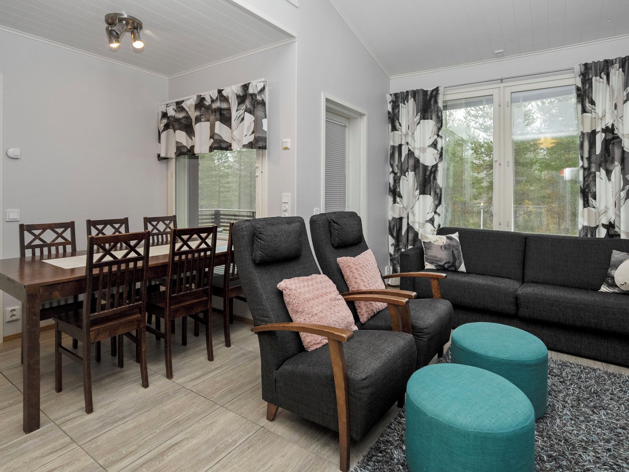 Ein modernes Wohnzimmer mit Essbereich, grauen Sofas, Holzstühlen und einem türkisblauen Ottomanen.