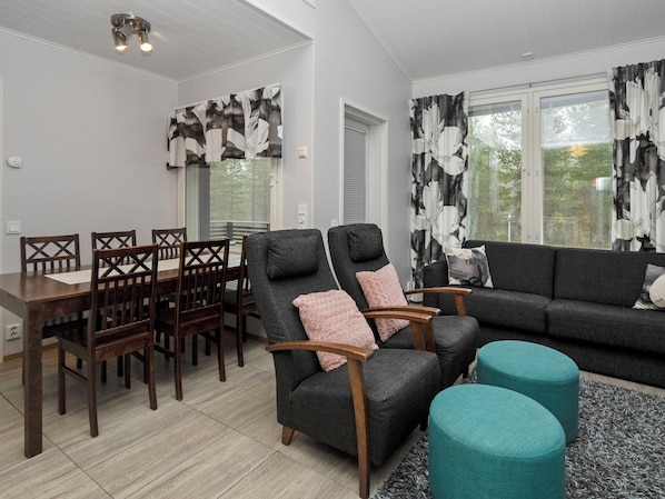 Un salon moderne comprenant un coin repas, des canapés gris, des chaises en bois et un pouf turquoise.