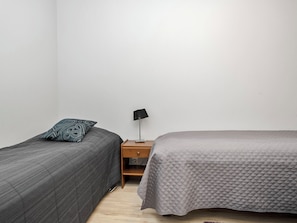 Une petite pièce simple, avec deux lits, une table de chevet et une lampe.