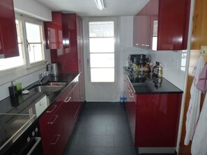 Eine kompakte Küche mit roten Schränken, einer Edelstahl-Spüle und einem Fenster, das für natürliches Licht sorgt.