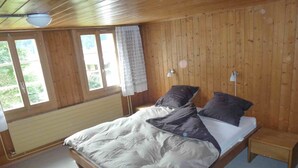 A wooden-paneled bedroom with a bed, a nightstand, and a window with a view of greenery.