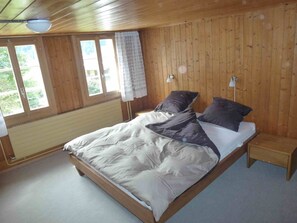 Ein Schlafzimmer mit Holzwandverkleidung, einem Bett, einem Nachttisch und einem Fenster mit Blick auf Grünflächen.