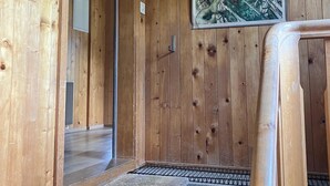 Een houten interieur met een schilderij van een berglandschap, een deur en een klein vloerkleed bij de ingang.