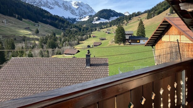 Berglandschap met besneeuwde toppen, een houten chalet en uitzicht vanaf een balkon.