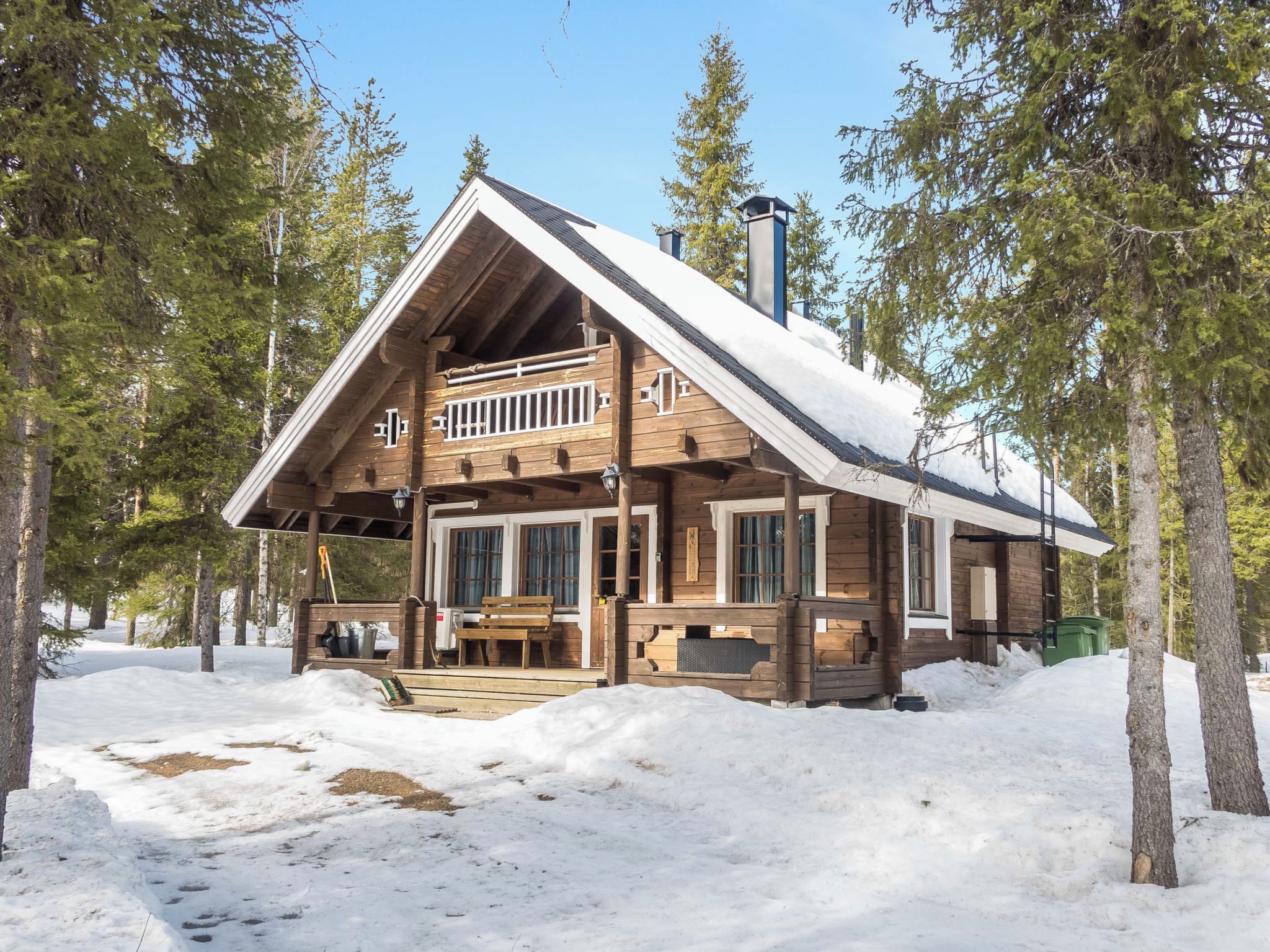 A wooden cabin with a balcony, surrounded by snow and trees.