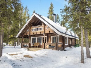 A wooden cabin with a balcony, surrounded by snow and trees.