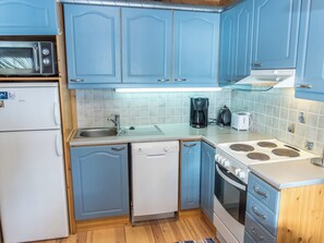 A compact kitchen with blue cabinets, a refrigerator, a dishwasher, a stove, and a coffee maker.