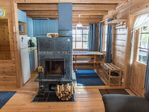 A cozy cabin interior with a stone fireplace, wooden furniture, and a kitchen area.